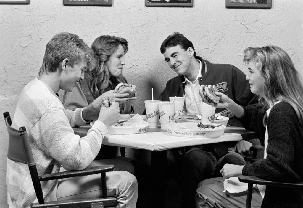 Zwei Paare in den 1980er Jahren an einem Gruppentermin essen Burger kosten ein Date