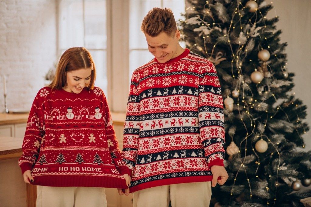 par, oblečen v božične puloverje pred drevesom