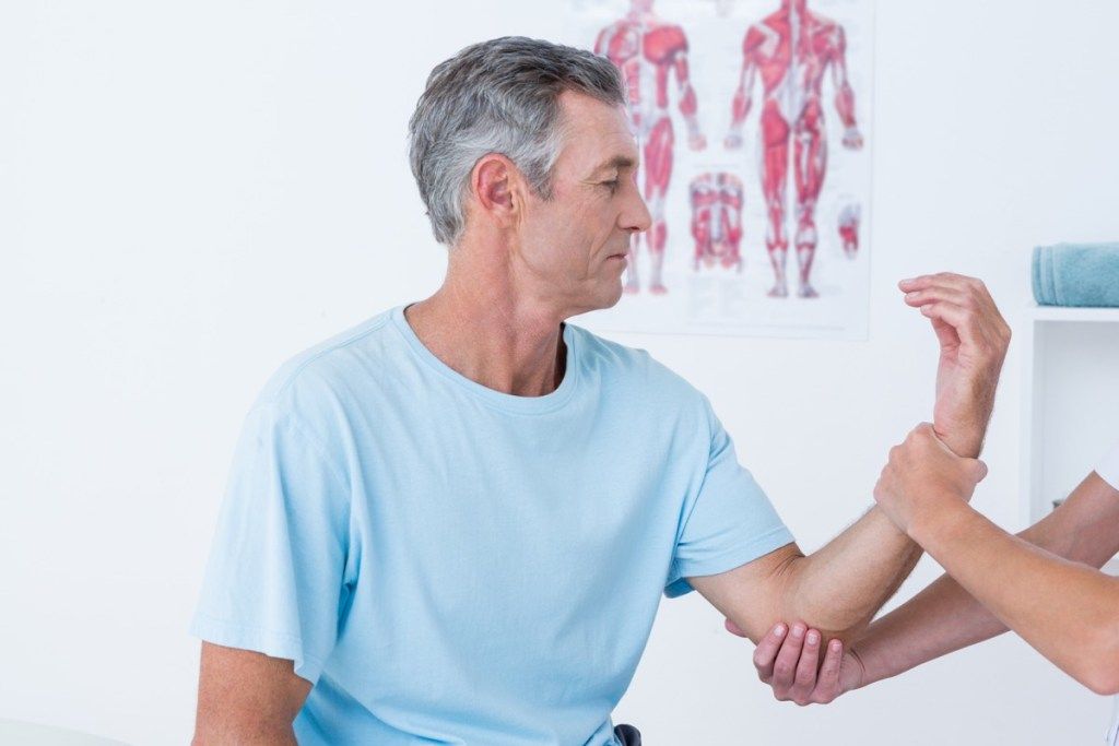 患者の筋肉を調べる医師、50歳以降の健康に関する質問