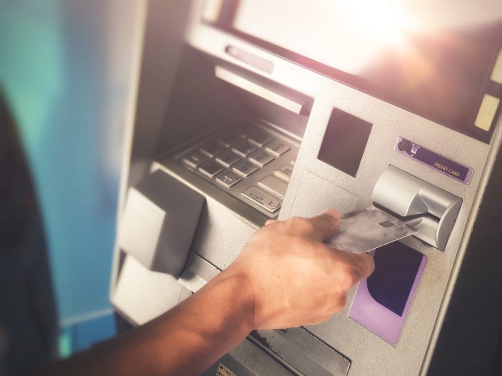 يد رجل تُدخل بطاقة ائتمان الصراف الآلي في آلة البنك لتحويل الأموال أو السحب - صورة