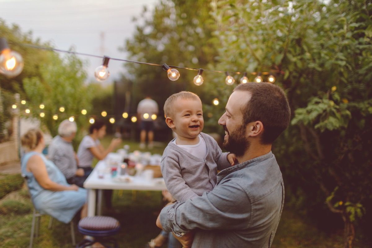 vit man håller baby och ler på utomhus fest