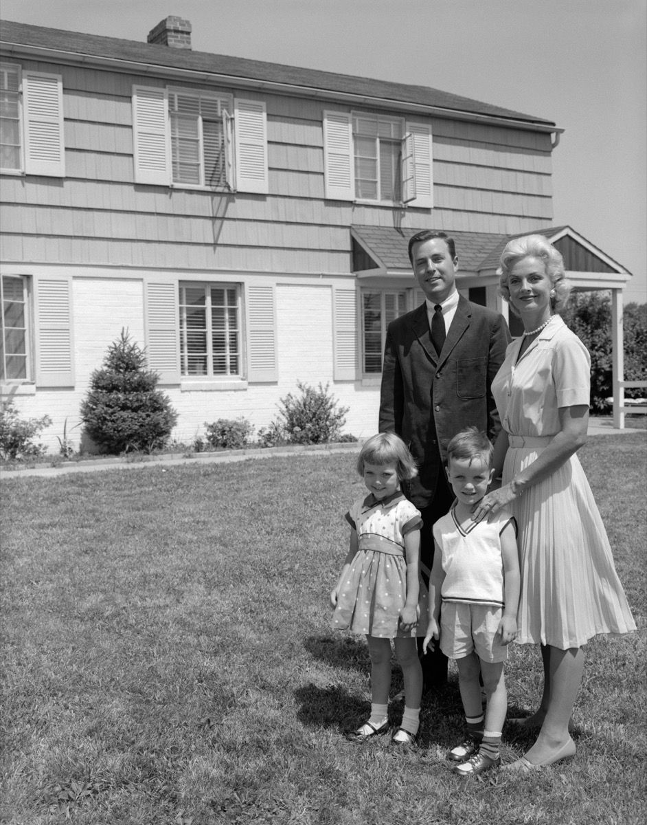 ครอบครัวชานเมืองปี 1960 ในรูปถ่ายขาวดำยืนอยู่หน้าบ้านหลังใหญ่ในย่านชานเมือง