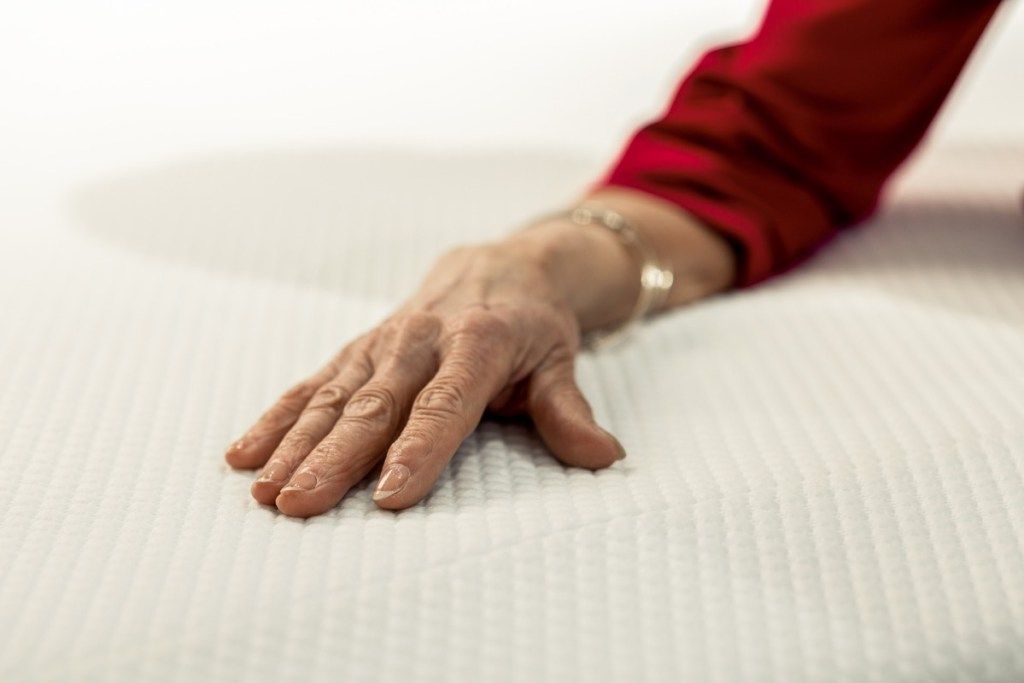 ηλικιωμένη γυναίκα που βάζει το χέρι της σε στρώμα αφρού μνήμης, καθημερινά είδη της NASA