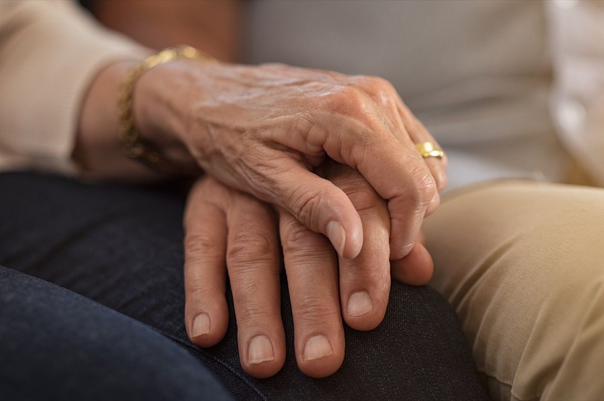 closeup pasangan lansia berpegangan tangan sambil duduk di sofa. Suami dan istri bergandengan tangan dan saling menghibur. Konsep cinta dan perhatian.