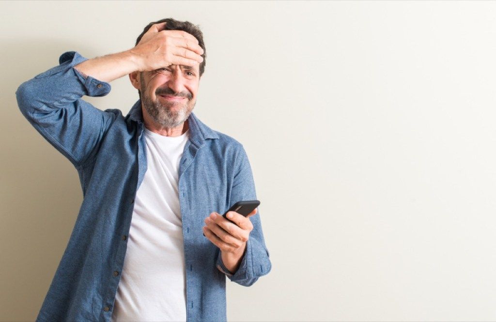 мъж на средна възраст, използващ смартфон, стресиран с ръка на главата