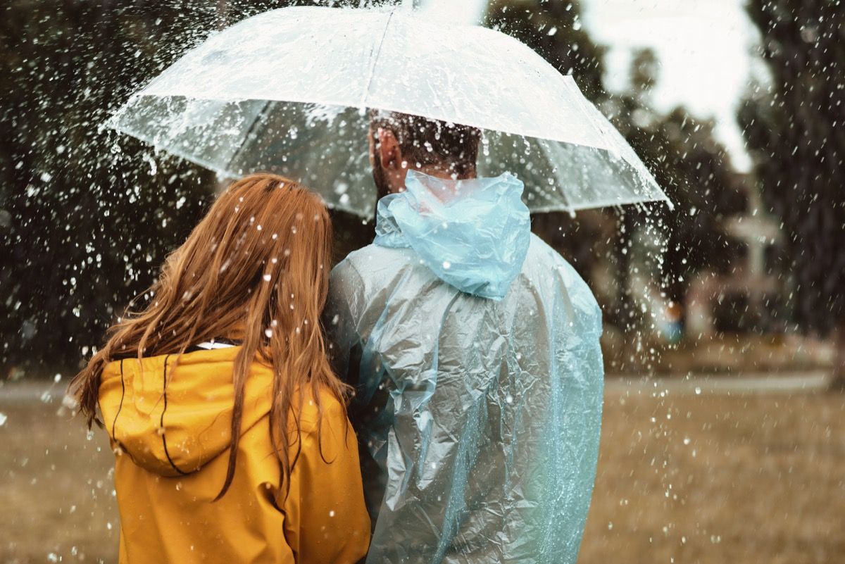 mies ja nainen kävelevät yhden sateenvarjon alla sateessa yhdessä