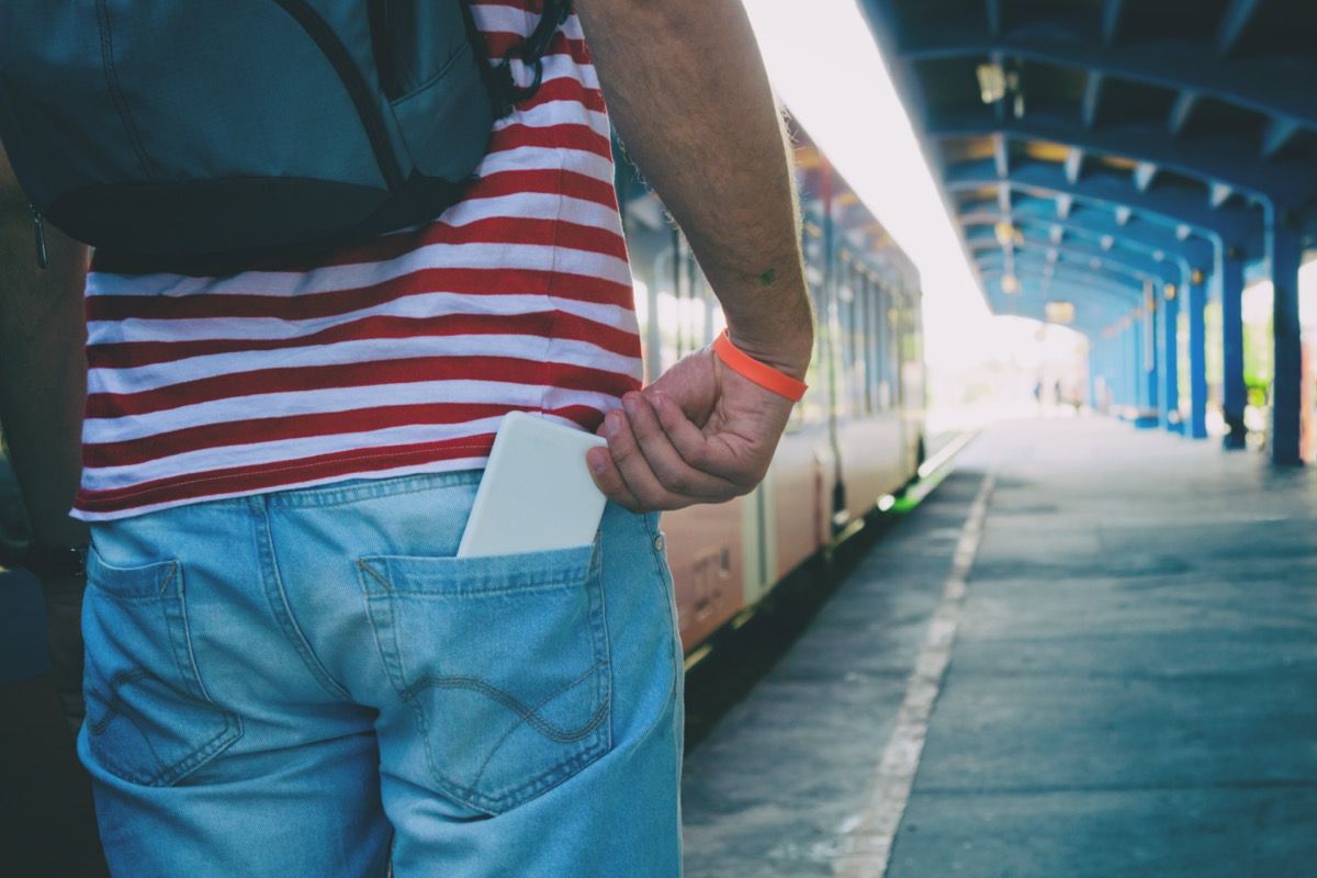 Hombre en la estación de tren con el teléfono en el bolsillo trasero