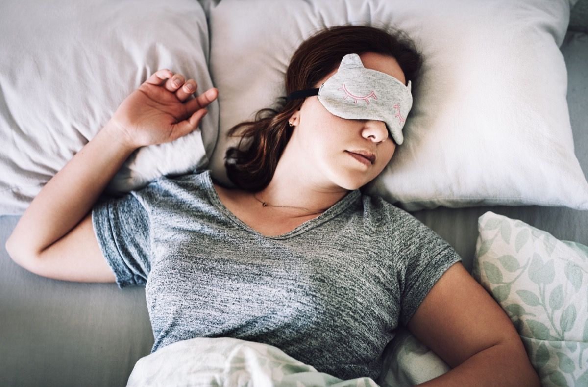 Posnetek privlačne mlade ženske, ki spi z masko na obrazu v svoji spalnici doma