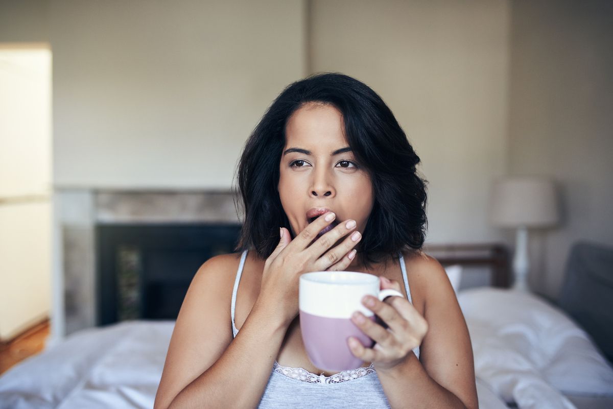امرأة شابة تتثاءب أثناء تناول القهوة في الصباح في المنزل