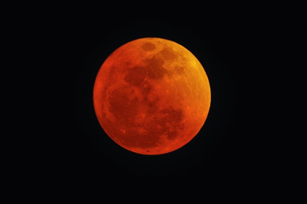 En rød og oransje måne på den mørke nattehimmelen