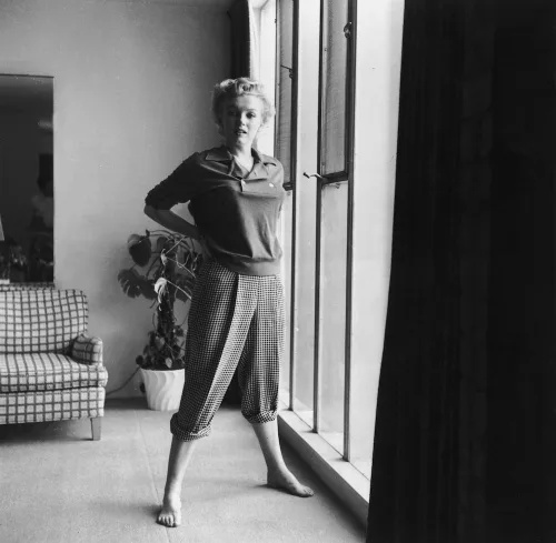   Merilina Monro fotografējās džemperī un rūtainās biksēs pozē pie loga ap 1955.