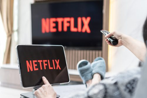   Osoba siedząca na kanapie i oglądająca Netflix na swoim telewizorze i tablecie
