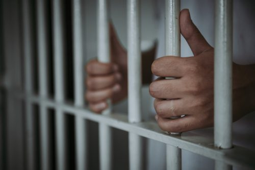   close-up de mãos segurando barras na prisão