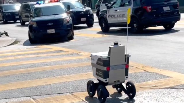 Video parāda, ka pārtikas piegādes robots ripo Losandželosas nozieguma vietā, kamēr nerimstoši policisti skatās