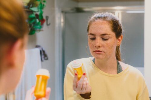 Žena v koupelně při pohledu na pilulku láhev