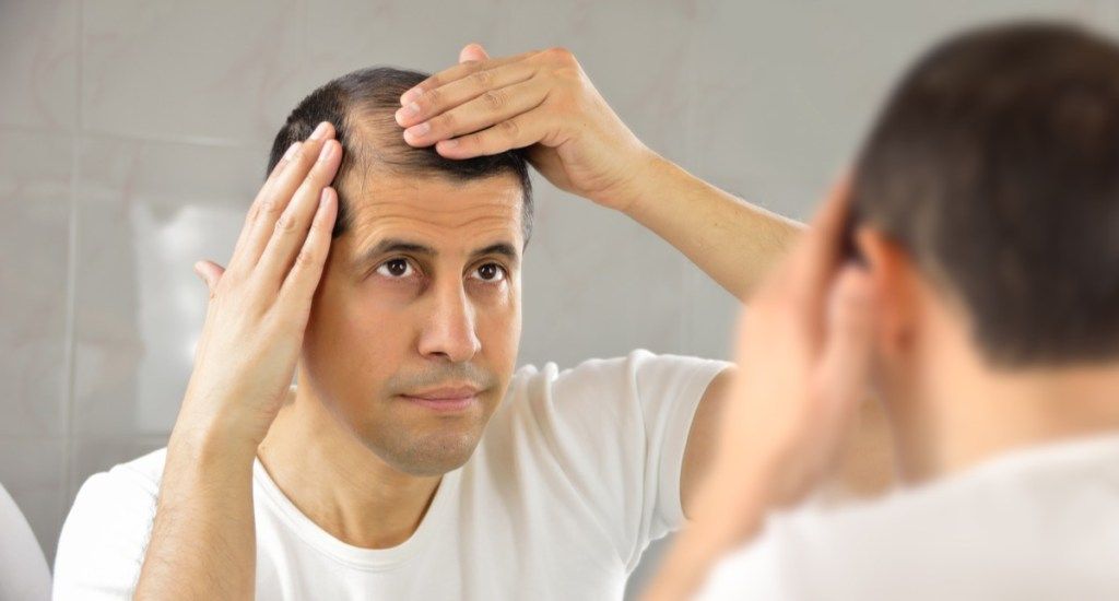 čovjek kontrolira gubitak kose i nesretan pogled u zrcalo