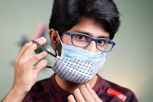 Junger Mann mit doppelter oder zweifacher Gesichtsmaske zum Schutz vor Coronavirus oder Covid-19-Ausbruch - Konzept von Sicherheit, Gesundheitswesen, Medizin und Hygiene.