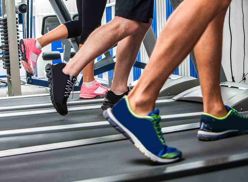 kojos ant bėgimo takelio vyras ir moteris, mankštinosi kardio treniruotes vyresniems nei 40 metų vyrams