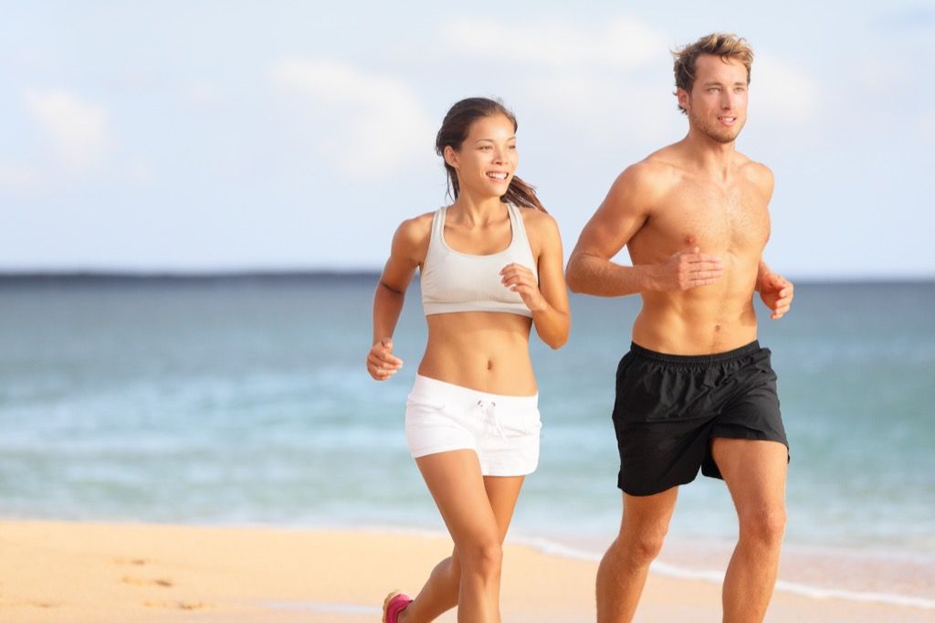 40 से अधिक पुरुषों के लिए कार्डियो वर्कआउट का अभ्यास करते हुए पुरुष और महिला युगल समुद्र तट पर दौड़ते हैं