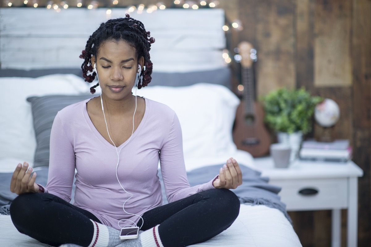 אישה שחורה מדיטציה והאזנה למוזיקה על מיטתה