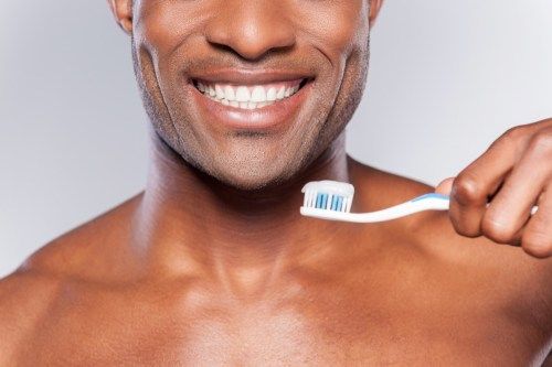 איש מחזיק מברשת שיניים עם משחת שיניים עליה בזמן שהוא מחייך