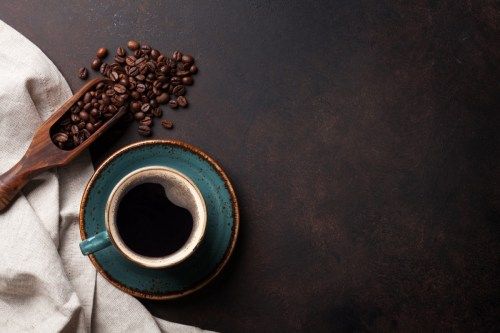 כוס קפה על צלוחית כחולה לצד פולי קפה וסקופית