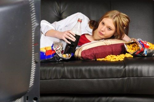 ילדה מנשנשת על הספה בזמן שהיא צופה בטלוויזיה