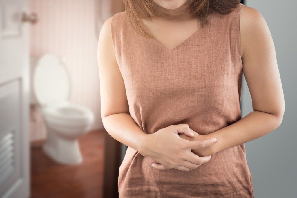 Mujer sosteniendo su estómago con dolor justo fuera del baño