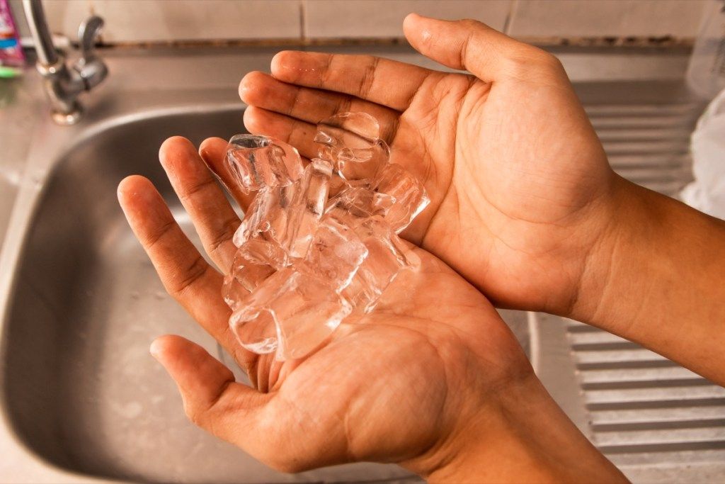 mâini albe ținând cuburi de gheață peste chiuvetă