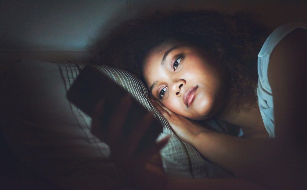 Снимак младе жене која ноћу користи мобилни телефон у кревету