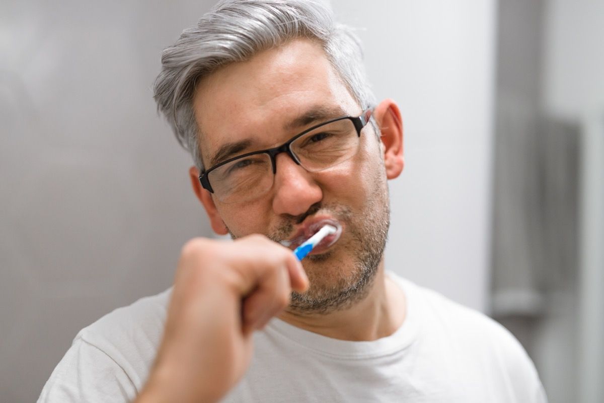 pria dengan rambut abu-abu sedang menyikat gigi