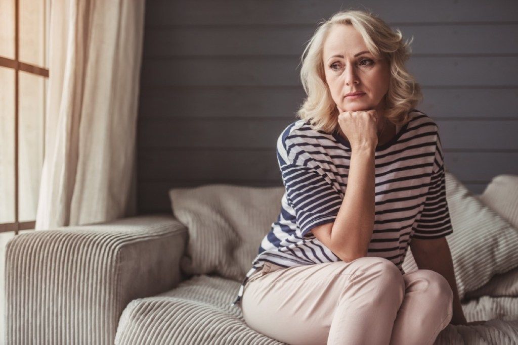 liūdna vyresnė balta moteris, sėdinti ant sofos
