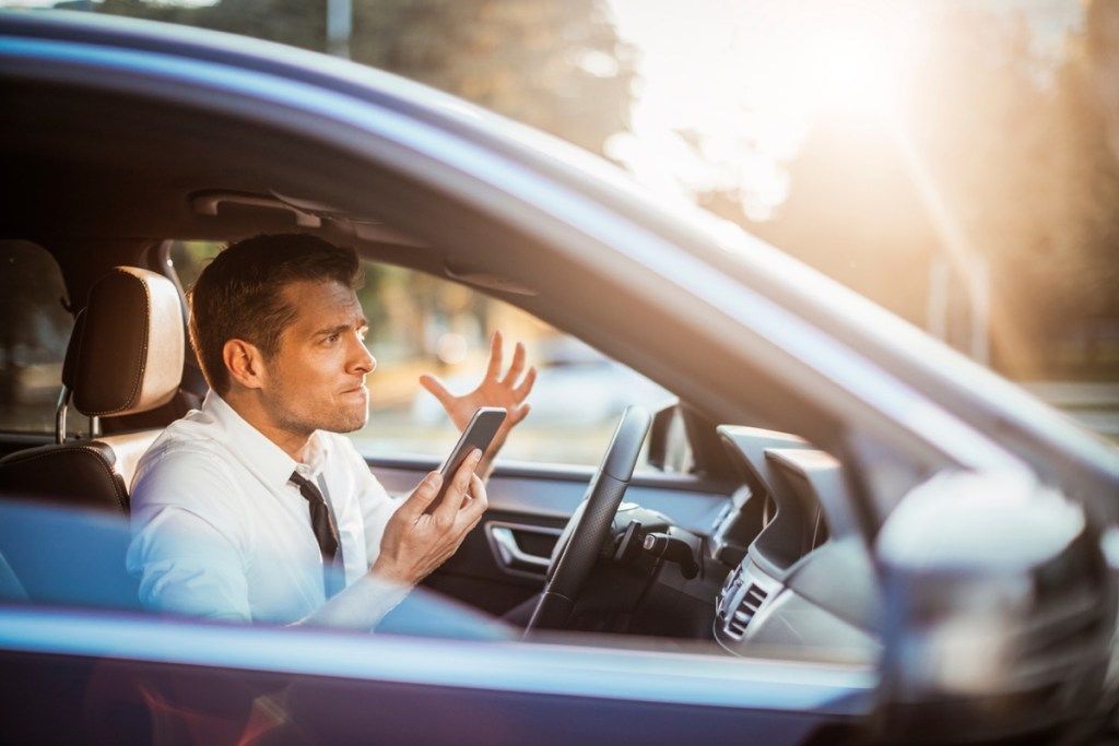 Крупным планом фото бизнесмена, кричащего на свой телефон во время вождения