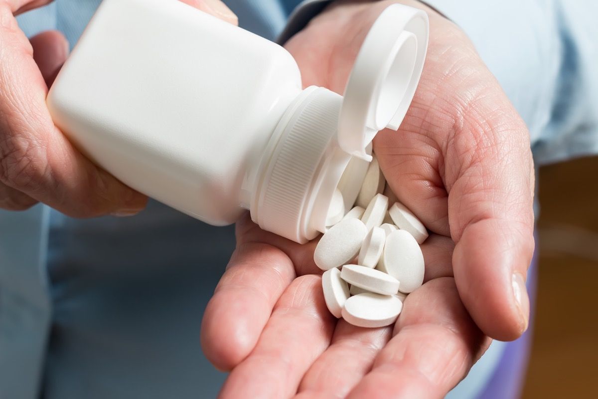 Tangan wanita memegang pil ubat putih, menuangkan dari botol putih ke telapak tangan suplemen makanan tablet kalsium.