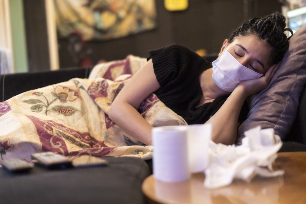 ผู้หญิงคนหนึ่งติดเชื้อไวรัสและป่วย นอนอยู่บ้านโดยใช้มาส์กหน้าผ้าเช็ดหน้าและกระดาษชำระบนโต๊ะ