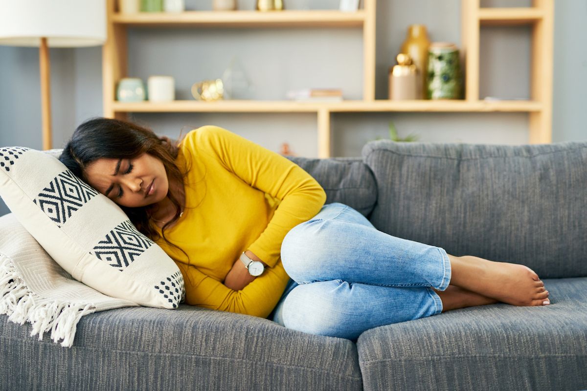 Mujer joven que sufre de calambres de estómago en casa en el sofá