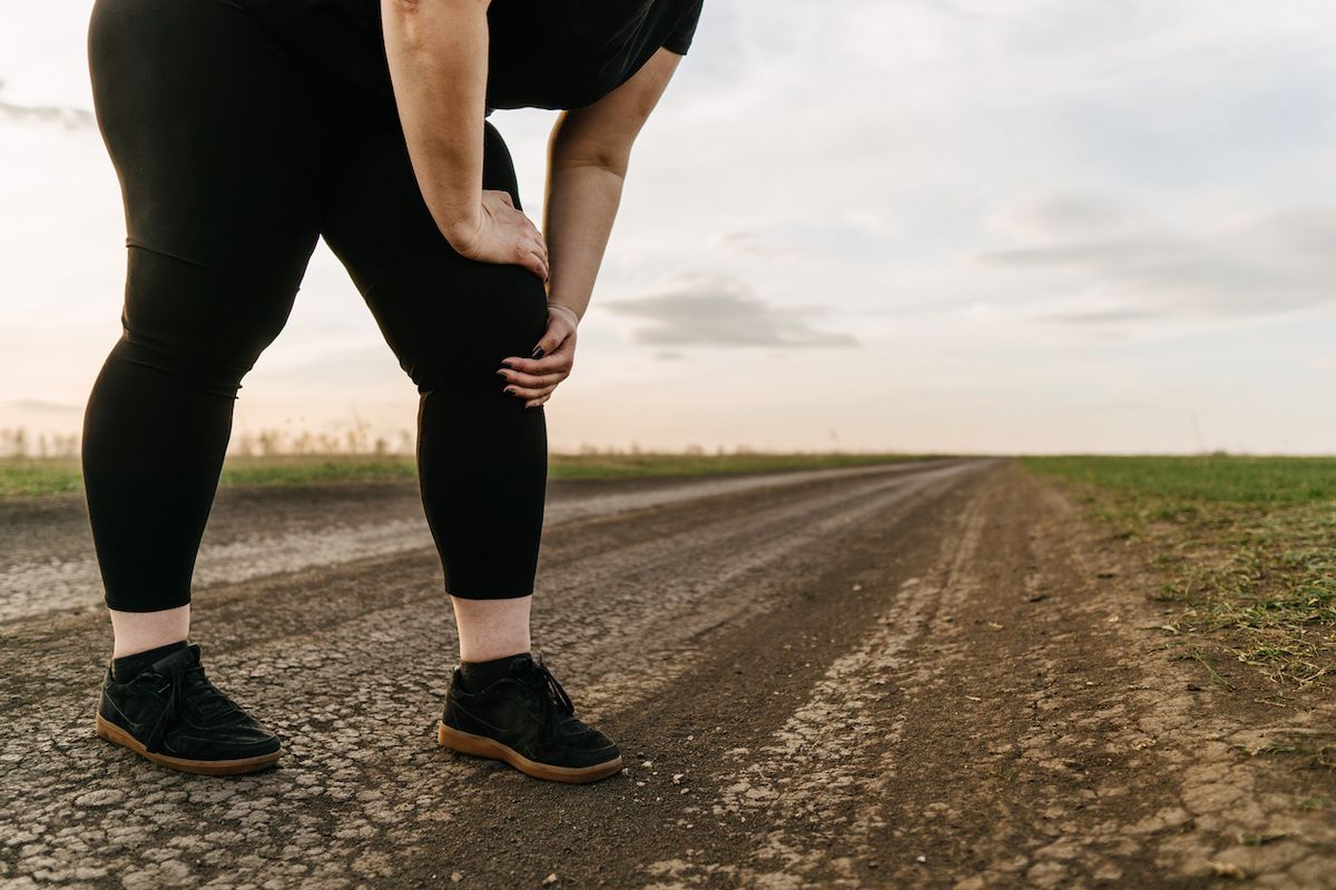 Ženska s prekomerno telesno težo se dotika bolečine v nogi