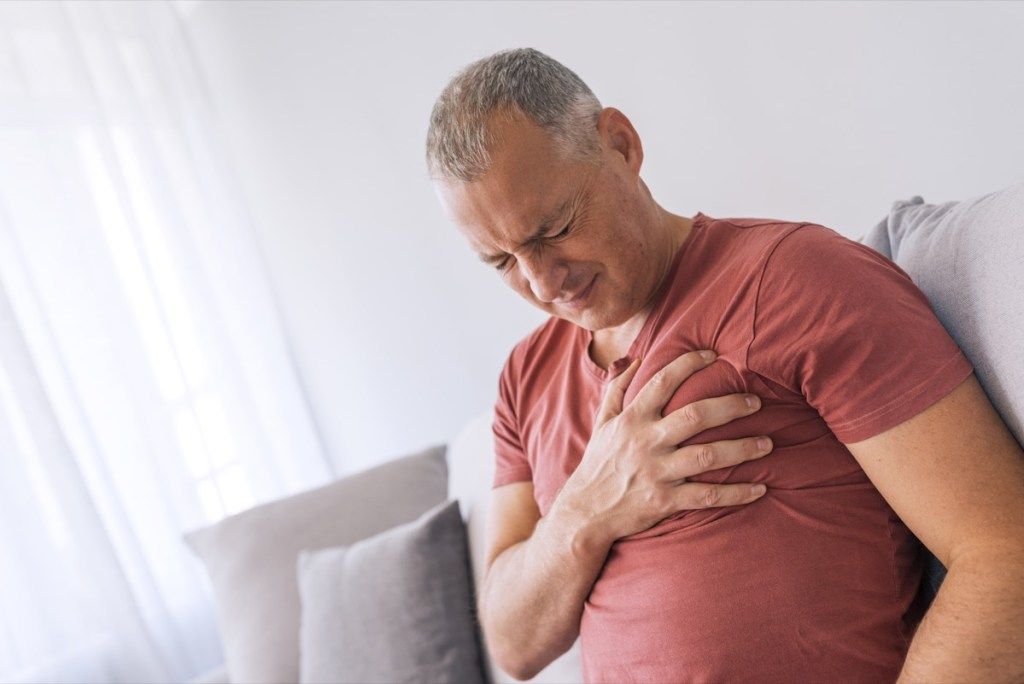 Vakava sydänsärky, mies, joka kärsii rintakipuista, jolla on sydänkohtaus tai tuskalliset kouristukset, painaminen rintaan kivulias ilme. Kuva kypsästä miehestä, joka kärsii rintakipuista kotona päivän aikana.
