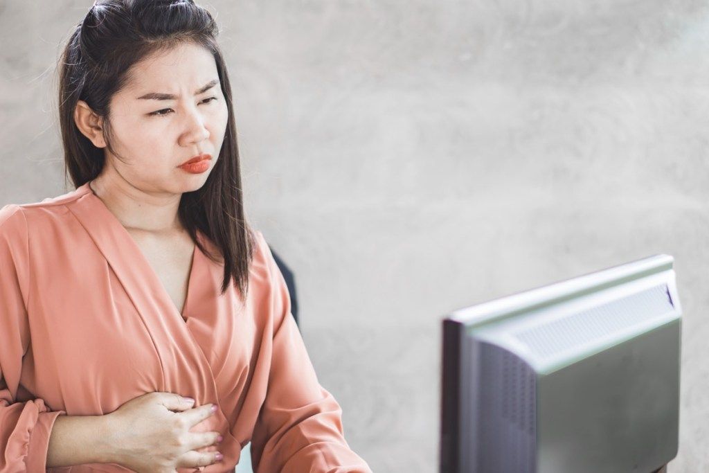 Kvinne som opplever ubehag i magen mens hun jobber på datamaskinen
