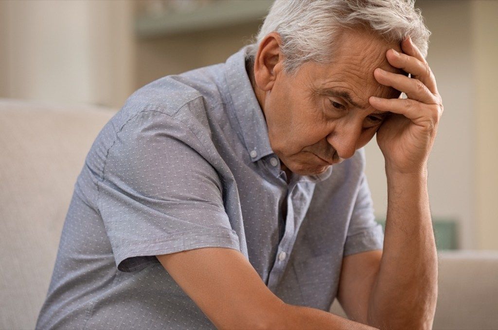huomaavainen vanhempi mies istuu sohvalla. Masentunut surullinen mies, joka istuu kädellä päähän ajattelemalla katseensa. Alzheimerista kärsivät vanhukset.