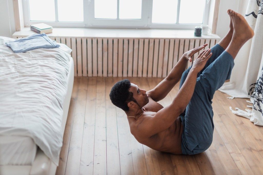 Mann macht Sit-ups zu Hause auf dem Boden seines Schlafzimmers
