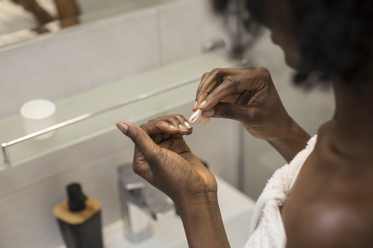 Mujer negra mira las uñas mientras se quita el esmalte de uñas.