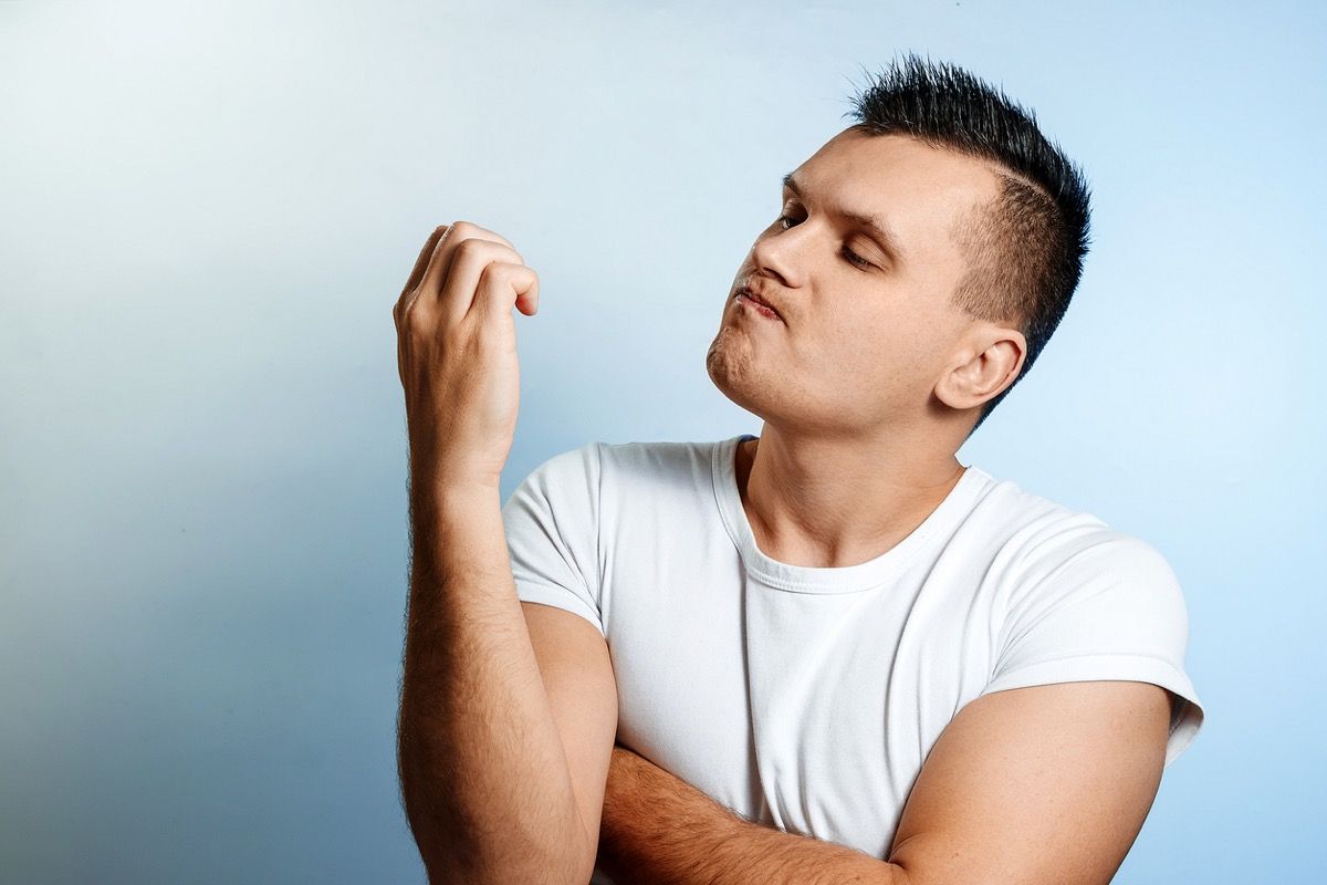 Retrato de un hombre blanco sobre un fondo claro, mirando sus uñas.