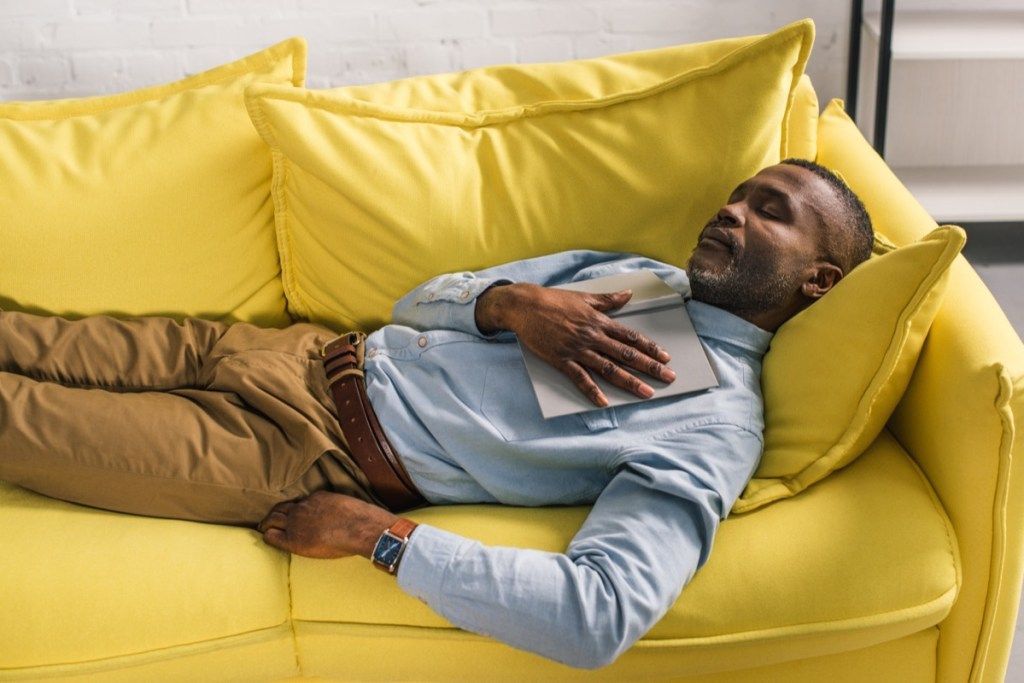 Anciano negro en pantalones caqui y botón para dormir la siesta en el sofá amarillo bajar la presión arterial naturalmente