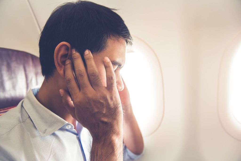 एक हवाई जहाज पर आदमी दर्द में अपने कान पकड़े हुए।