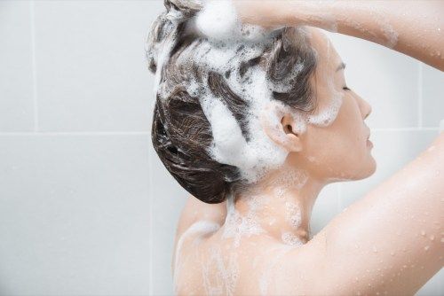 Kvinne som shampooer håret i dusjen