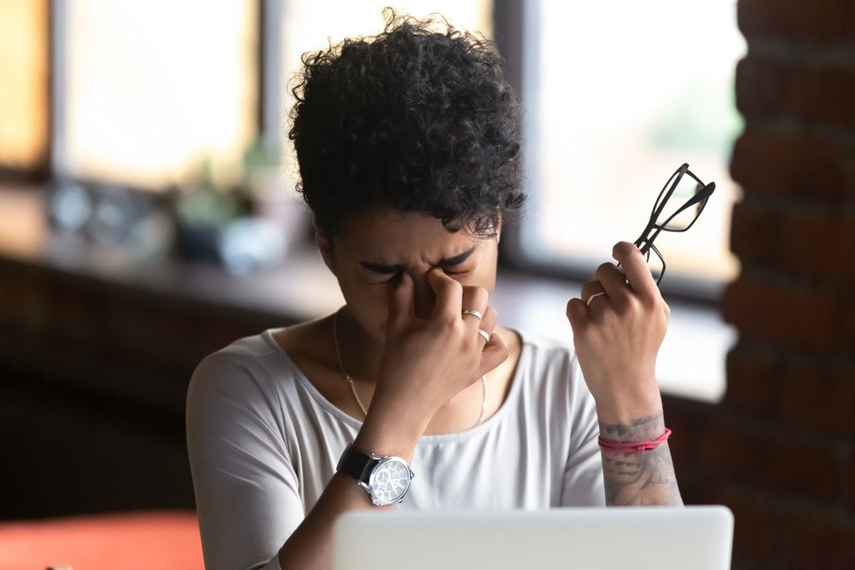黒人女性が目をこすり、コンピューターの前で眼鏡を持っている