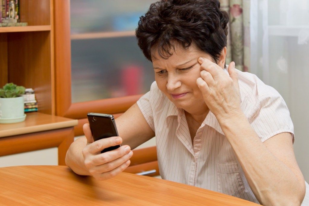 Жена, която присвива очи към телефона си, защото има проблеми със зрението