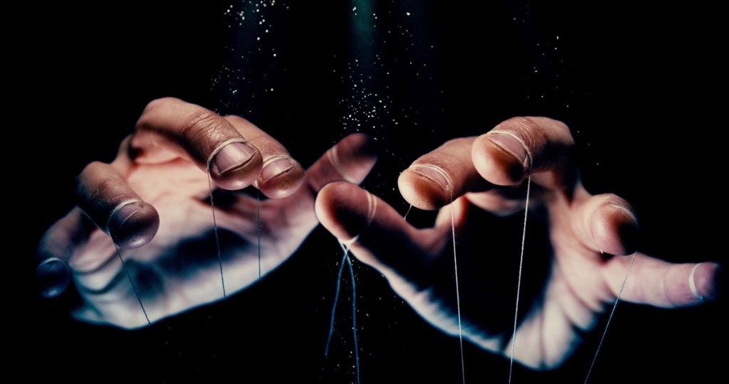 η φωτογραφία έννοιας ελέγχου με μαύρο φόντο δείχνει τα χέρια με κορδόνια δεμένα σε αυτά, όπως ένας μαριονέτα
