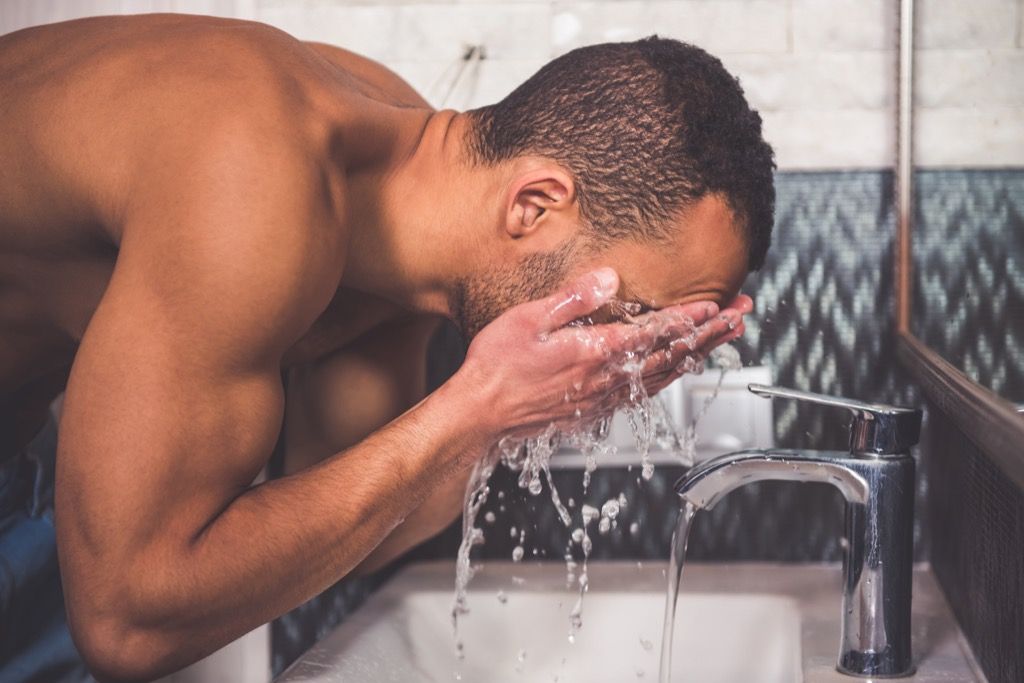 ผู้ชายล้างหน้าที่อ่างล้างหน้าในห้องน้ำ
